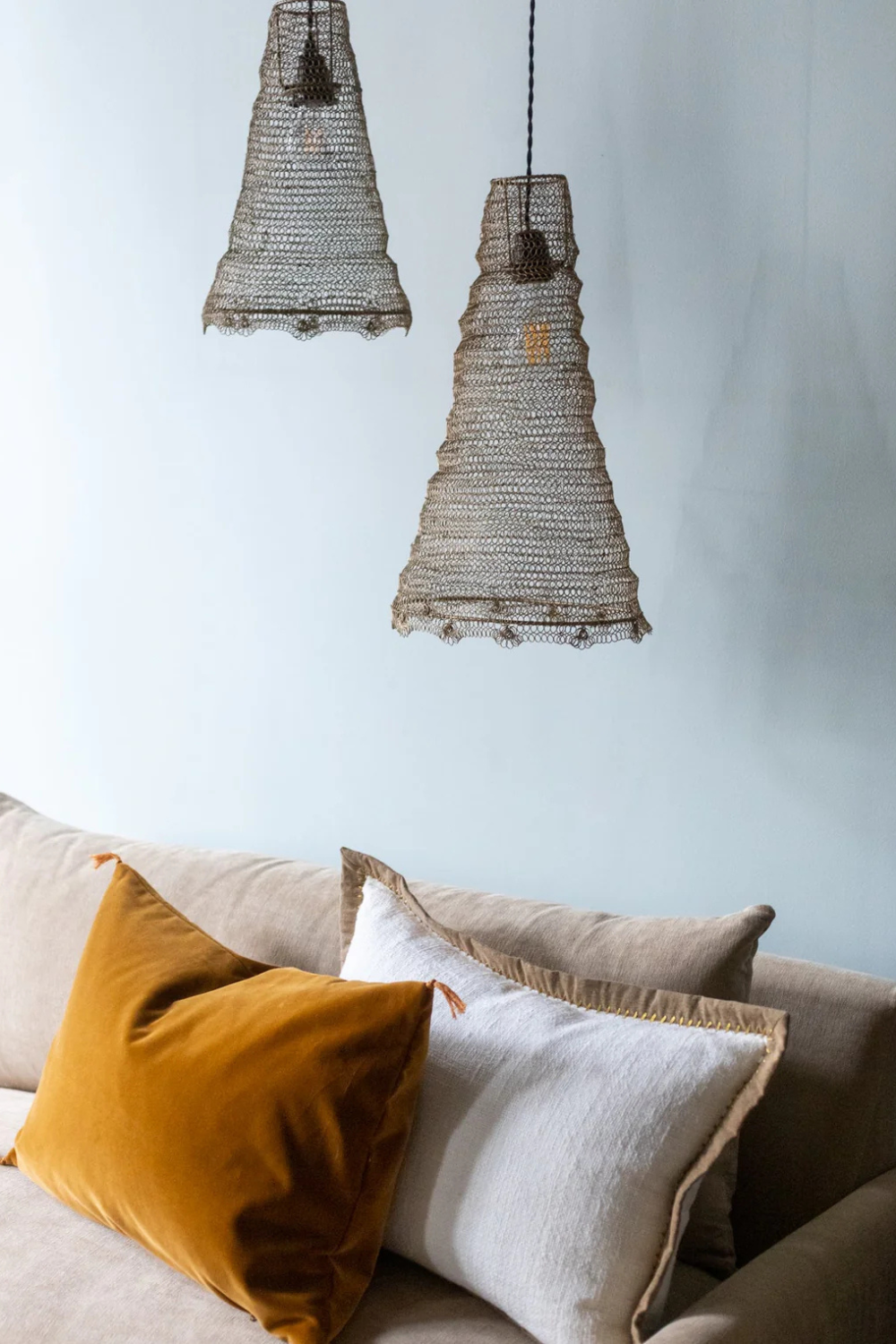 suspension-treccia-maison-couture-caravane-paris Salon cosy avec abat-jours en fibres naturelles et coussins en velours ocre et lin blanc sur canapé beige