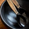 Avec les couverts à salade de la collection Souba, la lumière se glisse à table en douceur. Les manches ont été traités à chaud pour révéler un autre aspect de la corne. Et c’est ainsi que chaque couvert, pourtant composé d’une seule pièce, offre deux facettes : Le creux de la cuillère et de la fourchette, silhouettes naïves, brillent d’une satine noire. Le manche, à la teinte boisée, se veut mat et tendre au toucher. Un duo de couverts à salade bicolore, à la fois simple et moderne, d’une élégance parfaite. Des pièces réalisées à la main, dotées d’un charme au naturel déconcertant. C’est la promesse de composer une table unique, sans frontières.